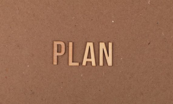 Wooden letters spelling 'PLAN' on a textured cardboard background with ample copy space.